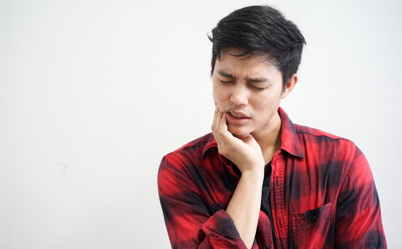 A man wearing a red plaid shirt rubs his jaw due to TMJ pain.