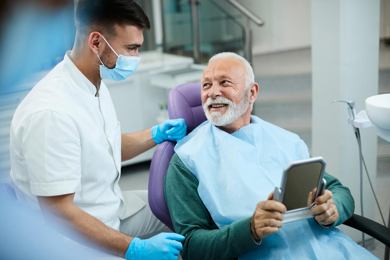 Older man sitting in a dental chair holding a small mirror and talking to the dentist Older man sitting in a dental chair holding a small mirror and talking to the dentist