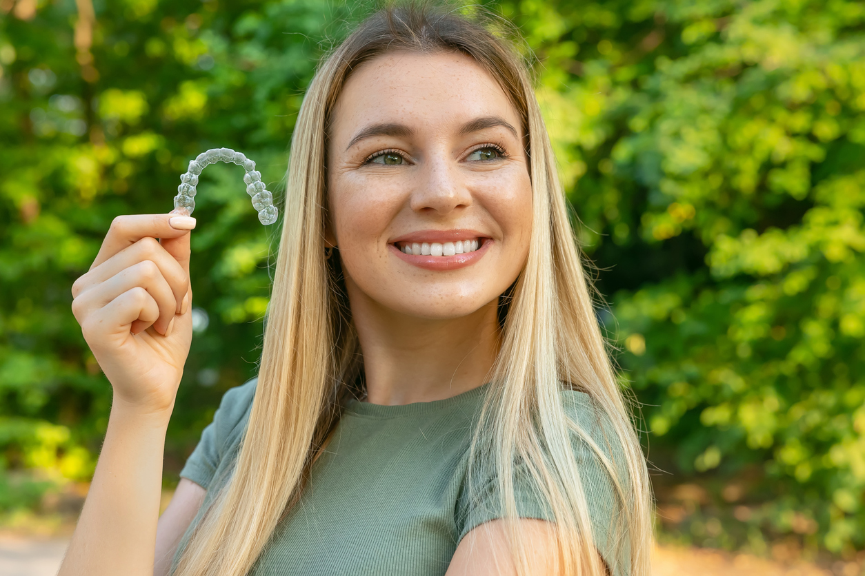 Woman holding Invisalign clear aligners while showing off her straighten smile