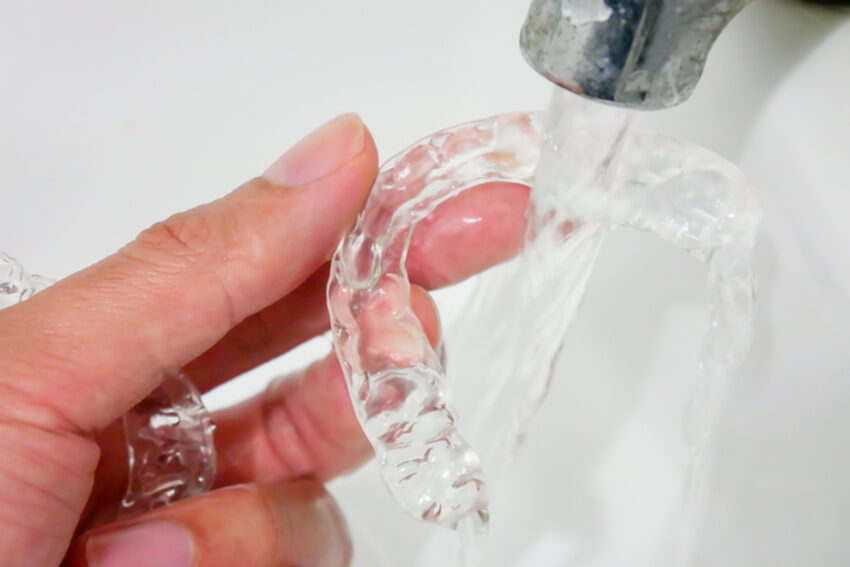 A person washing their clear dental aligners under running water